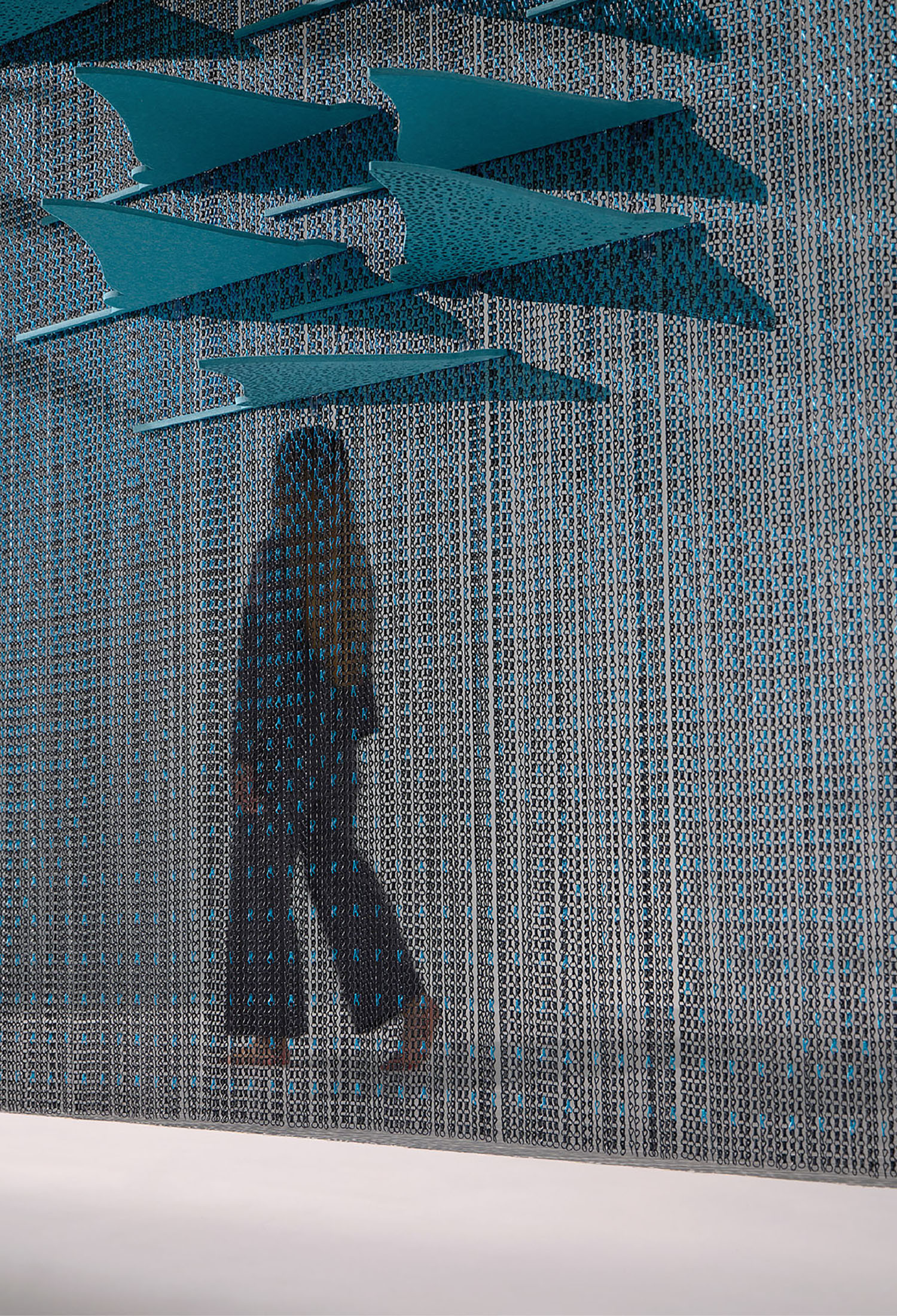 A person walking in front of a wall with a blue umbrella.