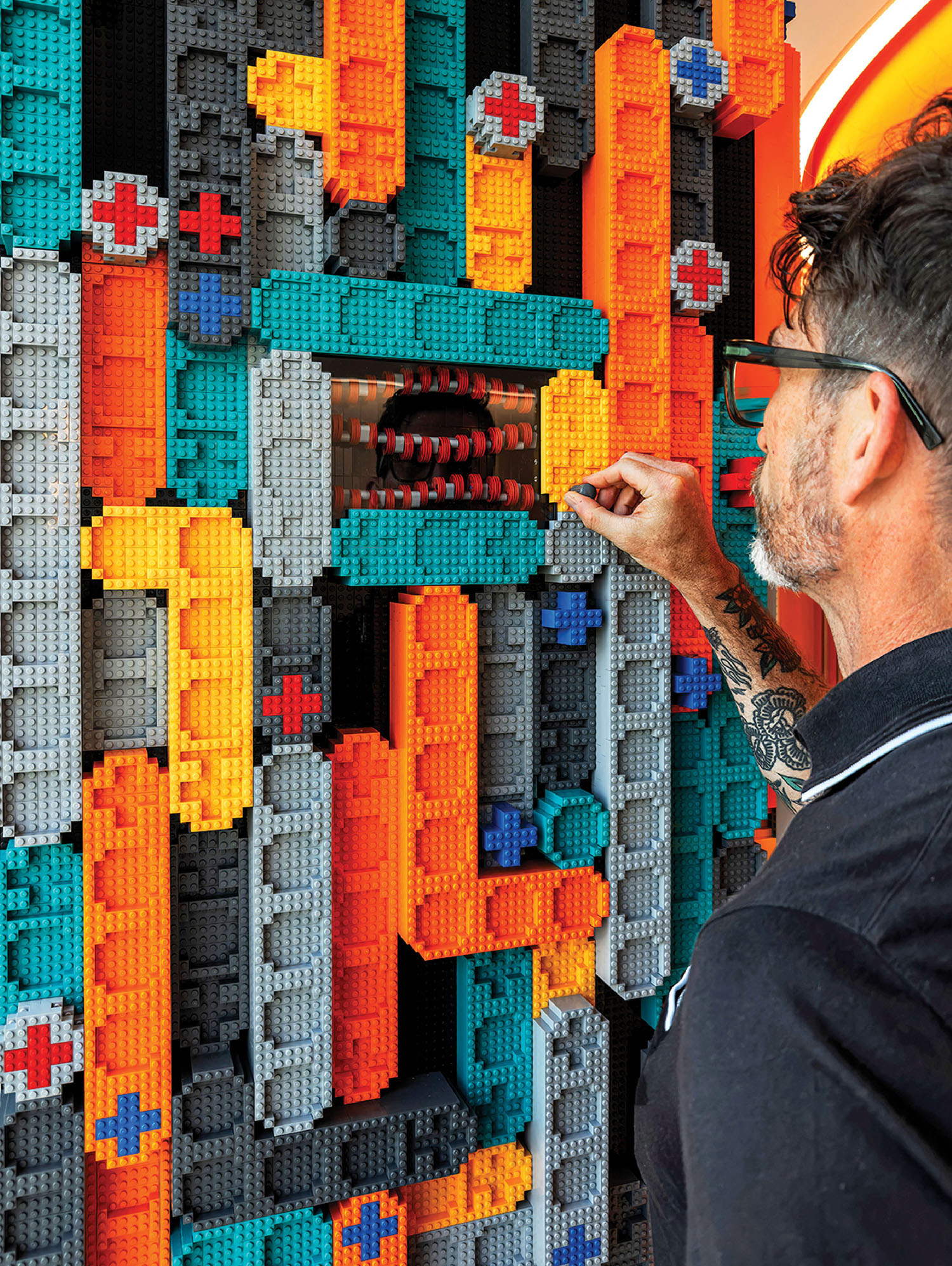 A man in a suit and sunglasses looking at a lego wall.