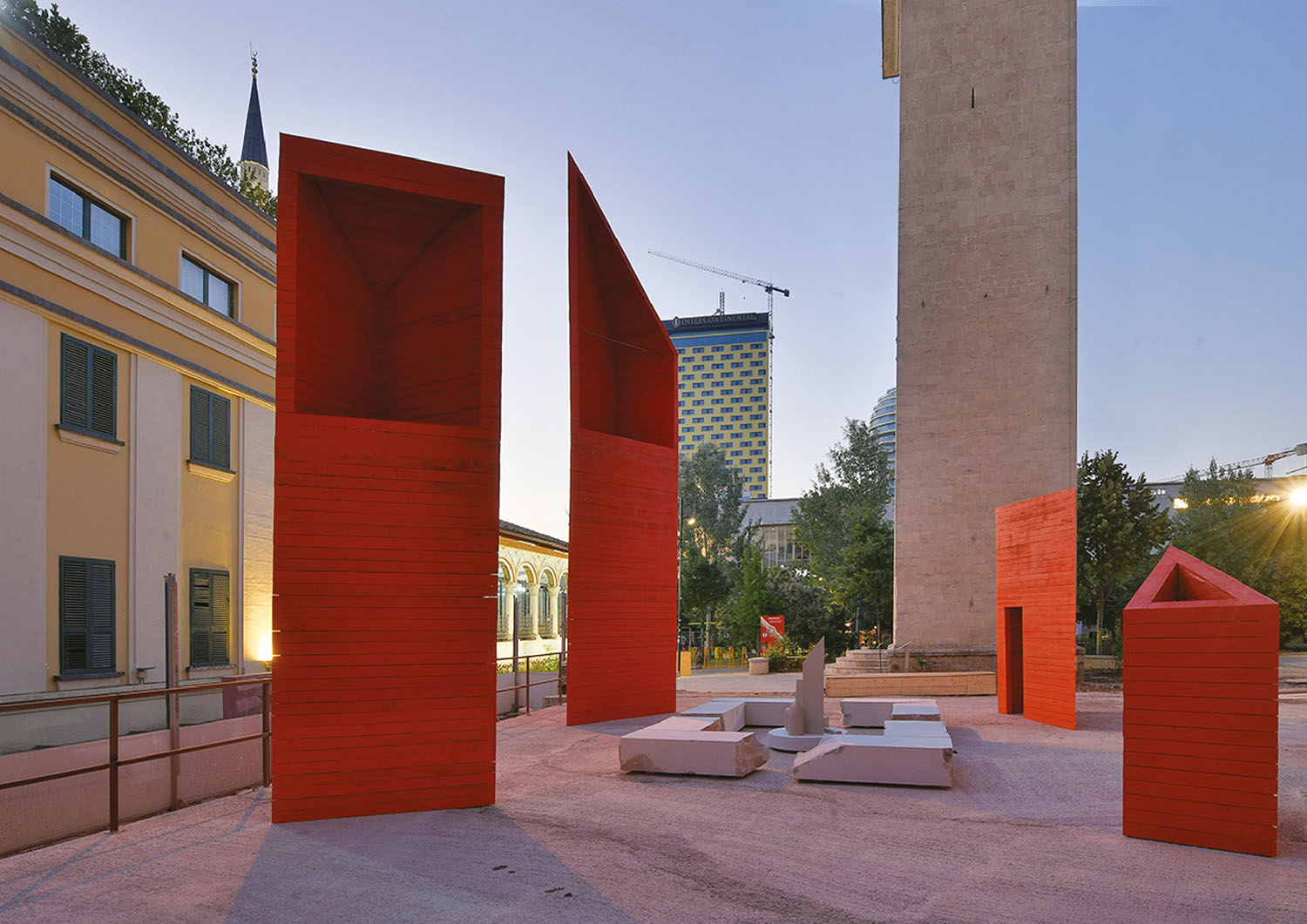 A red sculpture in a courtyard with a clock tower in the backgro.