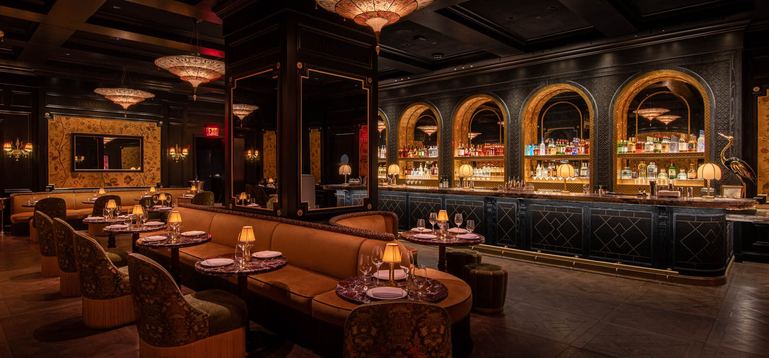 interior of restaurant with plush chairs, dark grey bar and chandelier lights